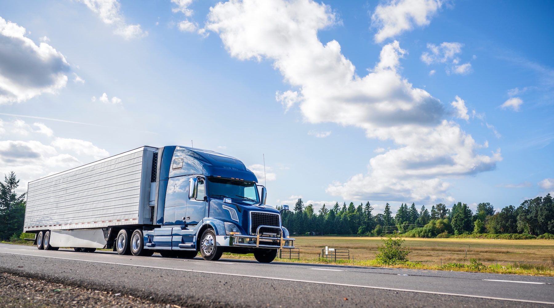 Blue big rig with white tractor load in front of a bright blue sky