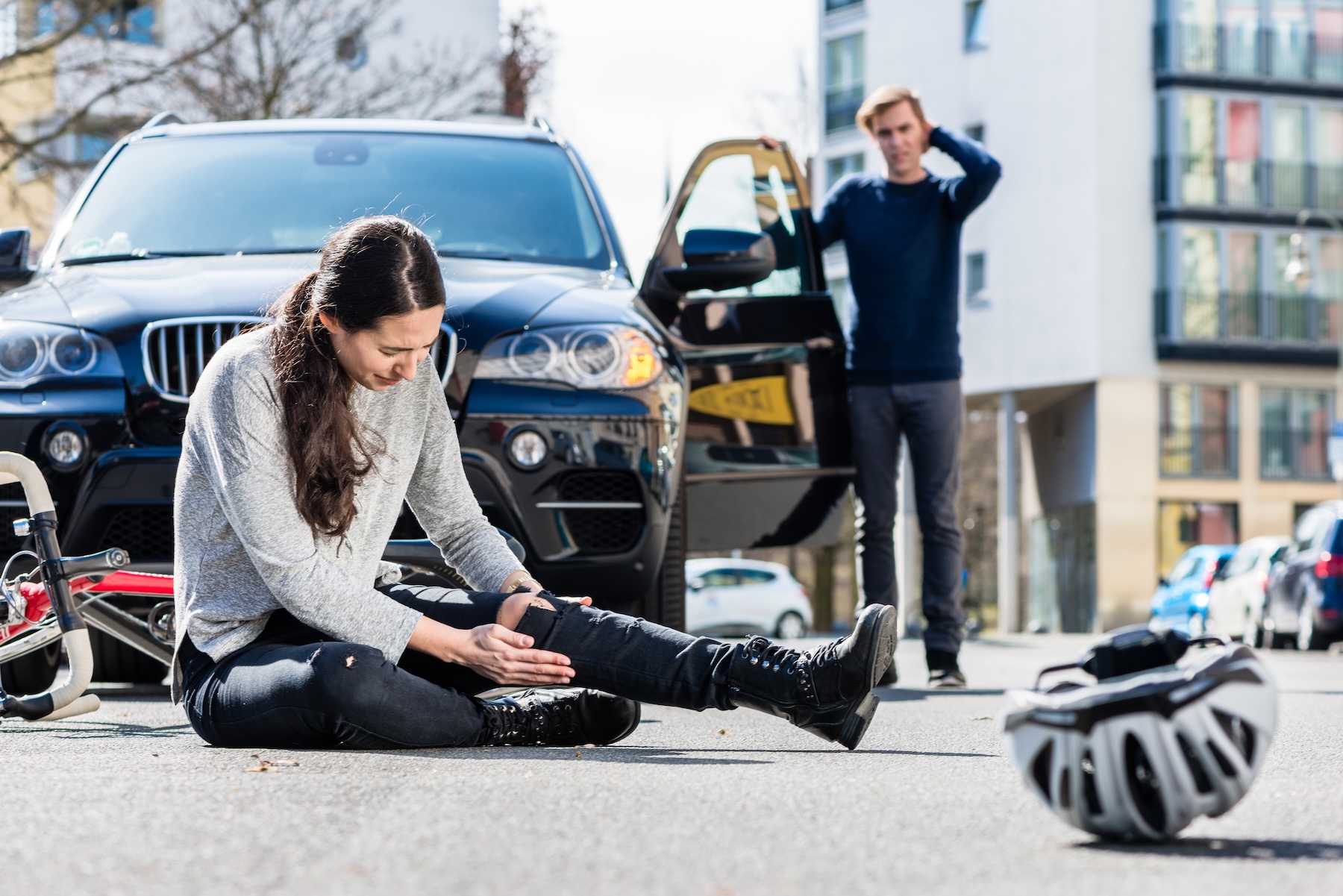 Young female bicyclist fallen down on street with serious injuries after traffic accident